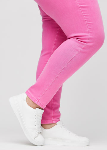 Slim-jeans til kvinner i lyserosa, fargen Flamingos. Nærbilde ved anklene på en plus size-modell, som viser passformen nederst på bena.