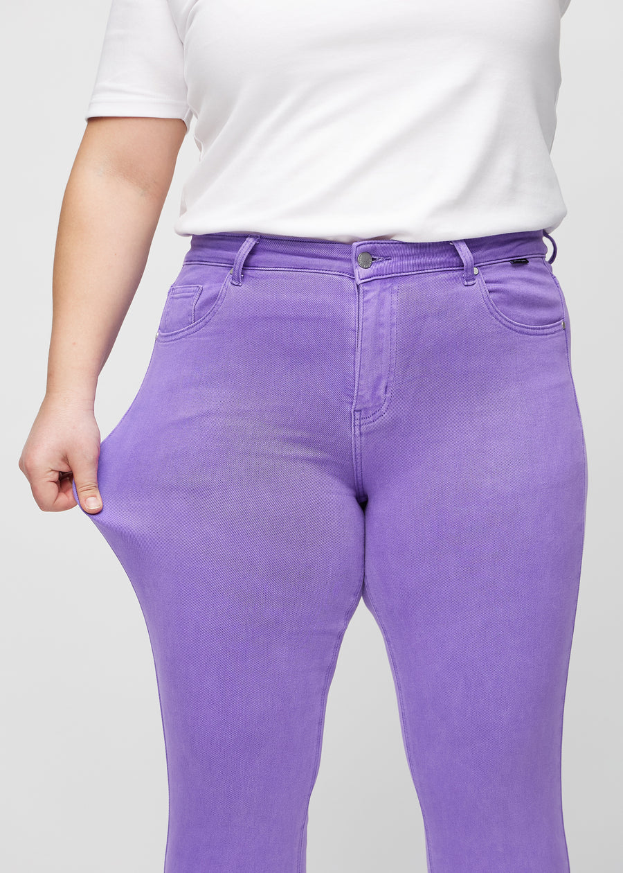 Slim-jeans til kvinner i lilla, fargen Lavenders. En plus size-modell strekker jeansstoffet ved låret for å vise stretchen.