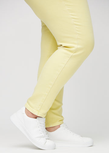 Slim-jeans til kvinner i lysegul, fargen Lemonades. Nærbilde ved anklene på en plus size-modell, som viser passformen nederst på bena.