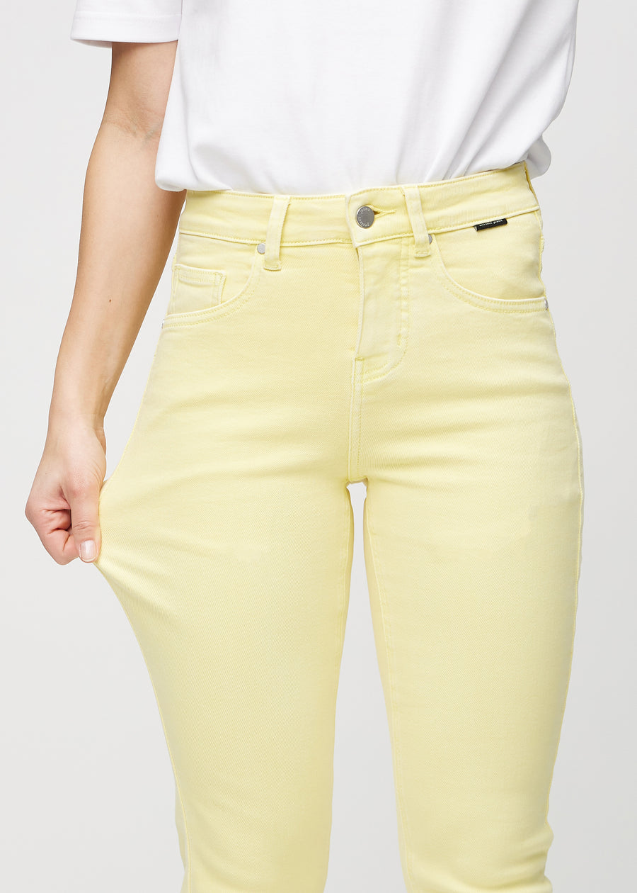 Slim-jeans til kvinner i lysegul, fargen Lemonades. En modell strekker jeansstoffet ved låret for å vise stretchen.