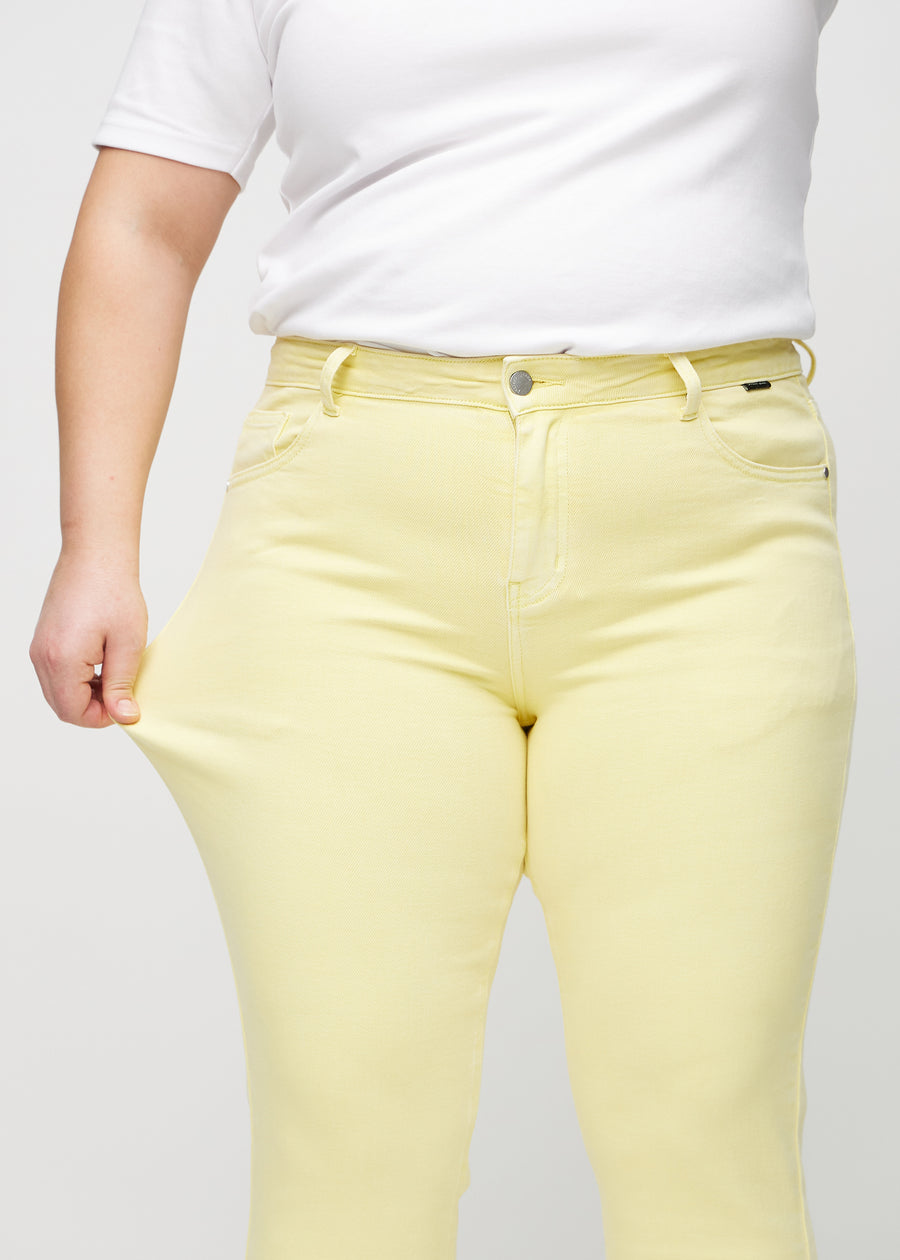 Slim-jeans til kvinner i lysegul, fargen Lemonades. En plus size-modell strekker jeansstoffet ved låret for å vise stretchen.