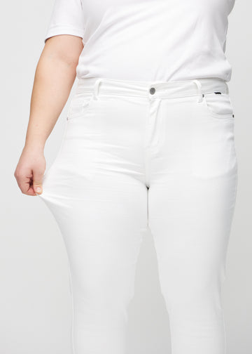 Slim-jeans til kvinner i hvit, fargen Marguerites. En plus size-modell strekker jeansstoffet ved låret for å vise stretchen.
