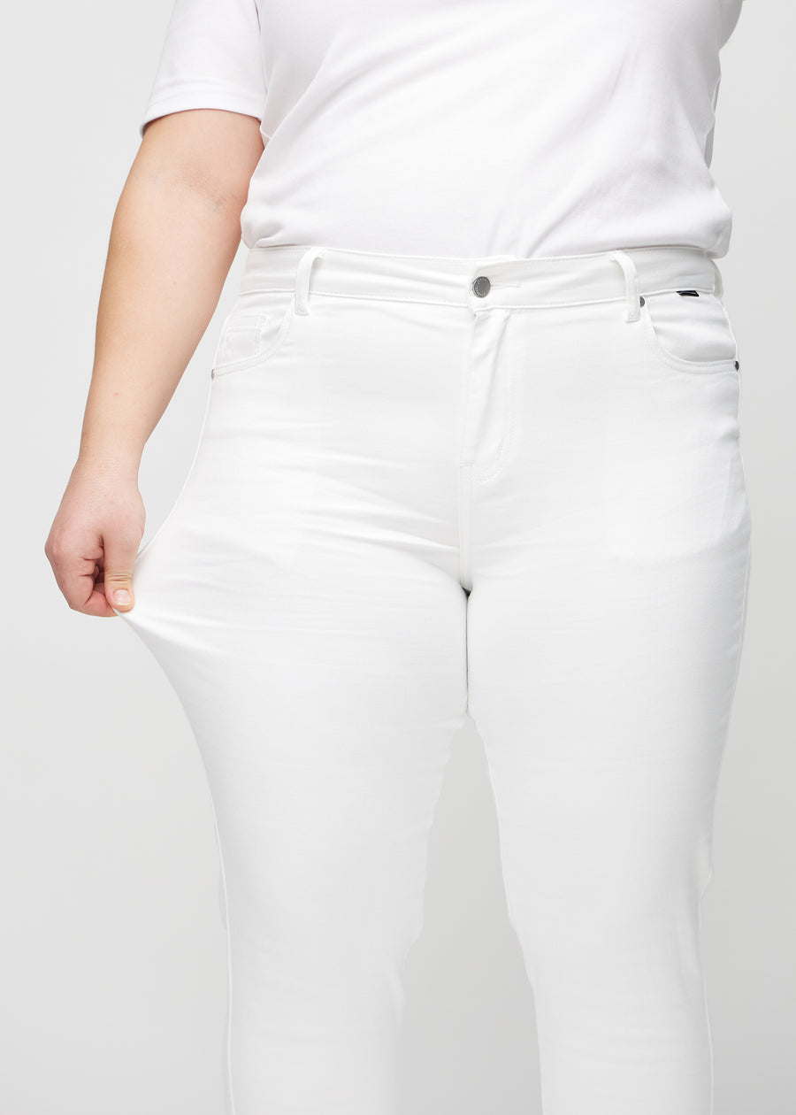 Slim-jeans til kvinner i hvit, fargen Marguerites. En plus size-modell strekker jeansstoffet ved låret for å vise stretchen.