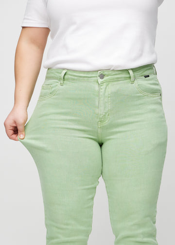Plus-size modell strekker jeansene ved låret for å vise stretch.