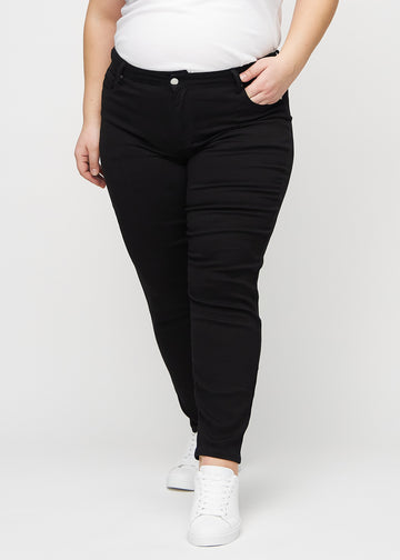 Svarte slim jeans, modellnavn Ravens, som sitter tett til benet, men litt løsere ved ankelen, på en plus-size-modell, sett forfra.