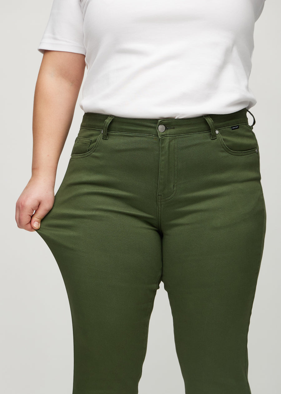 Slim-jeans til kvinner i mørkegrønn, fargen Renewals. En plus size-modell strekker jeansstoffet ved låret for å vise stretchen.