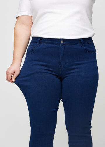Slim-jeans til kvinner i mørkeblå, fargen Royals. En plus size-modell strekker jeansstoffet ved låret for å vise stretchen.