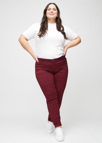 Slim-jeans til kvinner i mørkerød, fargen Santas. Helhetsbilde av en plus size-modell med jeansen på.