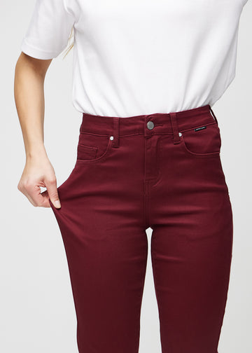 Slim-jeans til kvinner i mørkerød, fargen Santas. En modell strekker jeansstoffet ved låret for å vise stretchen.
