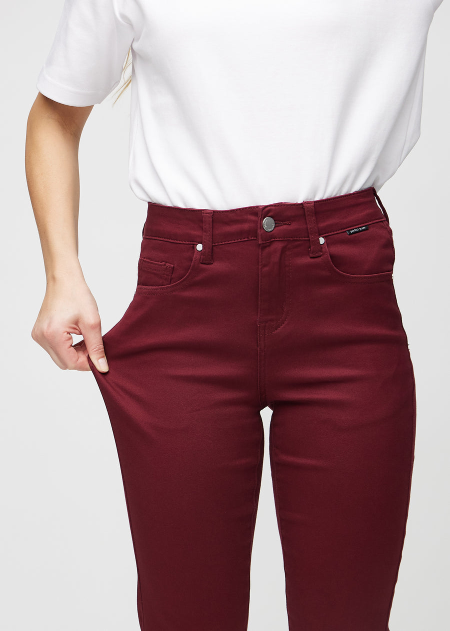Slim-jeans til kvinner i mørkerød, fargen Santas. En modell strekker jeansstoffet ved låret for å vise stretchen.