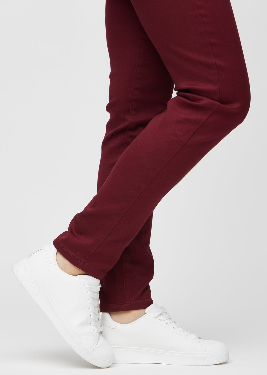 Slim-jeans til kvinner i mørkerød, fargen Santas. Nærbilde ved anklene på en modell, som viser passformen nederst på bena.