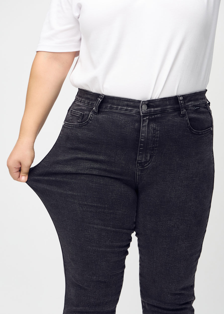Slim-jeans til kvinner i mørkegrå, fargen Shadows. En plus size-modell strekker jeansstoffet ved låret for å vise stretchen.