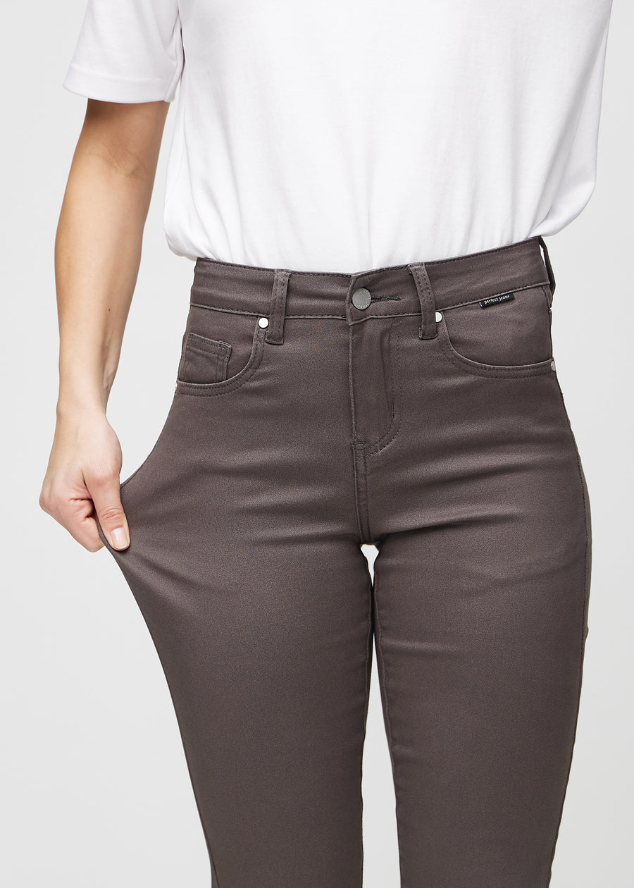 Slim-jeans til kvinner i gråbrun, fargen Thunders. En modell strekker jeansstoffet ved låret for å vise stretchen.