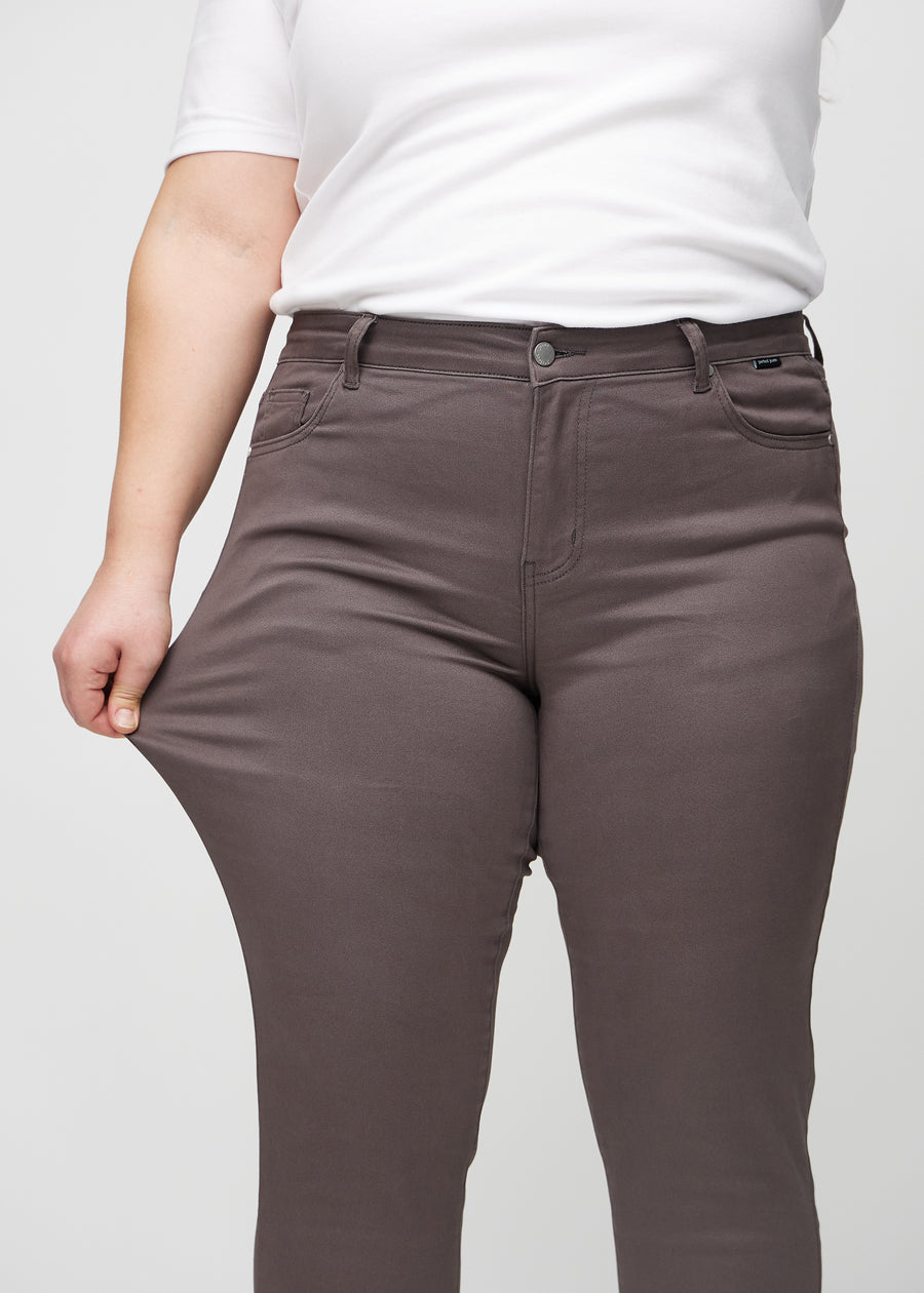 Slim-jeans til kvinner i gråbrun, fargen Thunders. En plus size-modell strekker jeansstoffet ved låret for å vise stretchen.