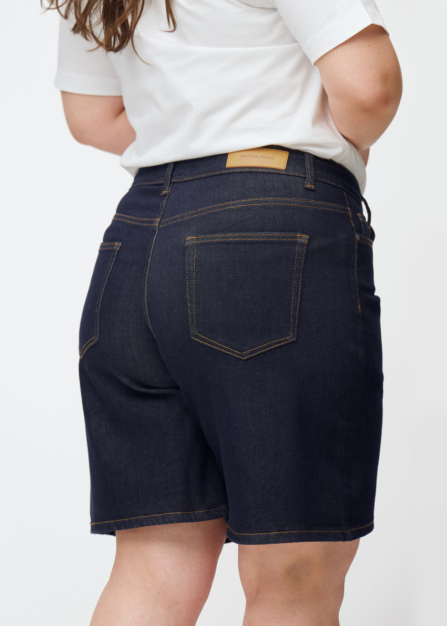 Dyp mørkeblå denimshorts til dame i fargen Midnights sett bakfra i nærbilde på plus-size modell.