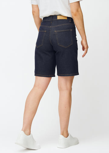 Dyp mørkeblå denimshorts til dame i fargen Midnights sett bakfra, slik at lengden rett over kneet vises.