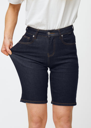 Modell strekker dyp mørkeblå denimshorts til dame i fargen Midnights ved låret for å vise materialets stretch.