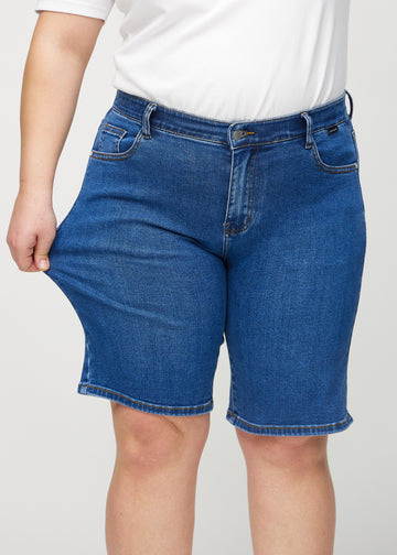 Plus-size modell strekker shortsen ved låret for å vise stretch.