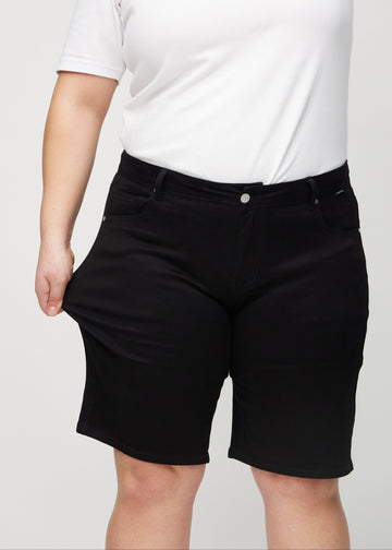Plus-size modellen strekker shortsen ved låret for å vise stretch.