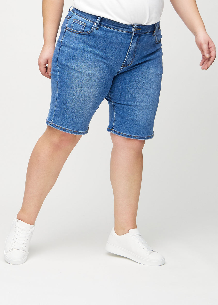 Denim regular middle shorts, modellnavn Rivers, som går rett ned langs benet og slutter rett over kneet på en plus-size-modell, sett forfra.