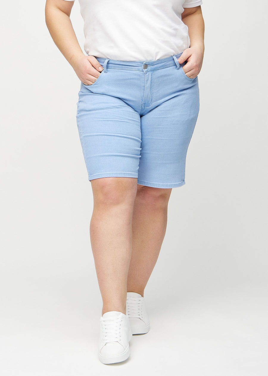 Lysblå regular middle shorts, modellnavn Skies, som går rett ned langs benet og slutter rett over kneet på en plus-size-modell, sett forfra.