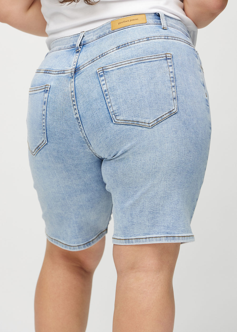 Lys denim regular middle shorts sett bakfra på nært hold på en plus-size modell for å vise detaljer.