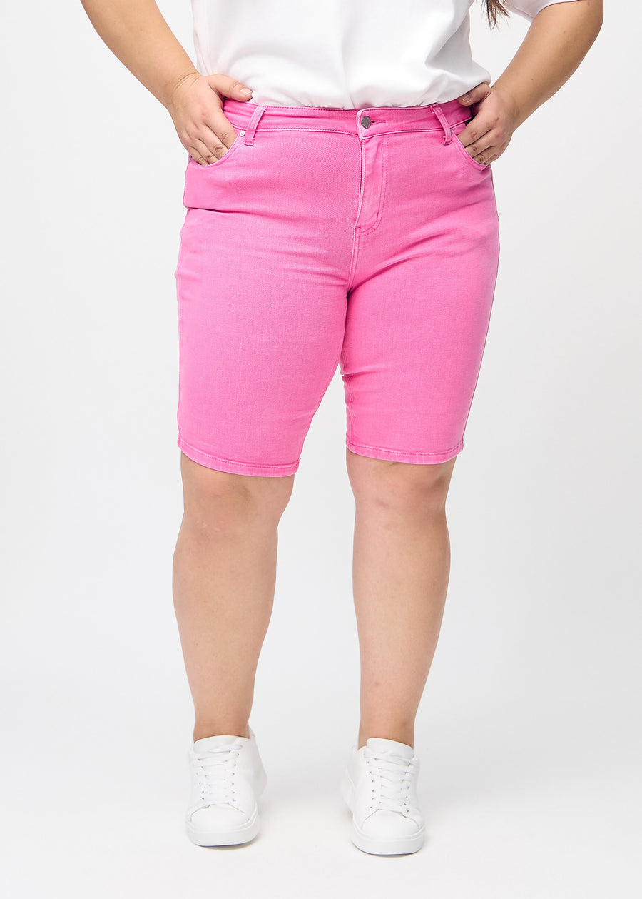 Lyserosa skinny middle shorts, modellnavn Flamingos, som sitter tett på låret og slutter rett over kneet på en plus-size modell, sett forfra.