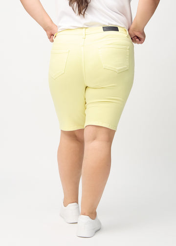Lysegule skinny middle shorts sett bakfra på en plus-size-modell, slik at man kan se hele produktet.