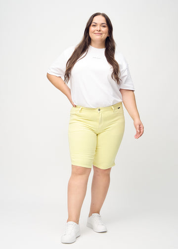 Fullt bilde av en plus-size-modell i lysegule skinny middle shorts.