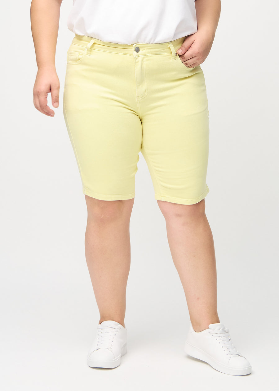Lysegule skinny middle shorts, modellnavn Lemonades, som sitter tett på låret og slutter rett over kneet på en plus-size-modell, sett forfra.
