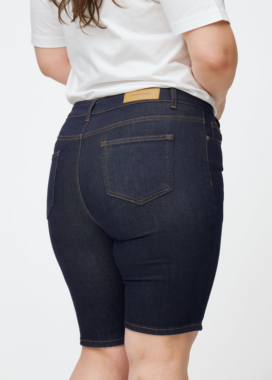 Dyp mørkeblå denimshorts til dame i fargen Midnights sett bakfra i nærbilde på plus-size modell.