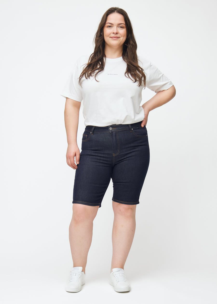 Helbilde av plus-size modell i dyp mørkeblå denimshorts til dame i fargen Midnights med skinny passform.