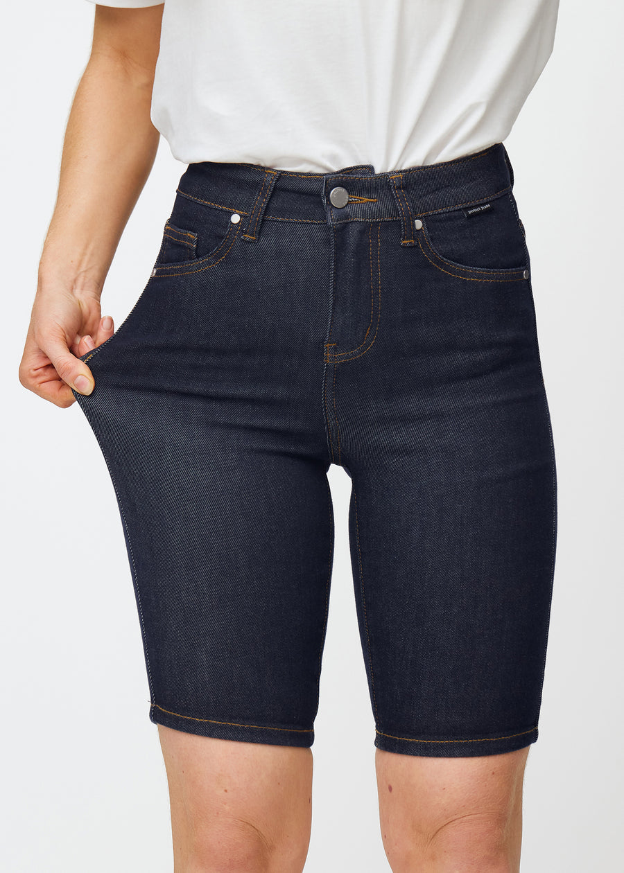 Modell strekker dyp mørkeblå denimshorts til dame i fargen Midnights ved låret for å vise materialets stretch.