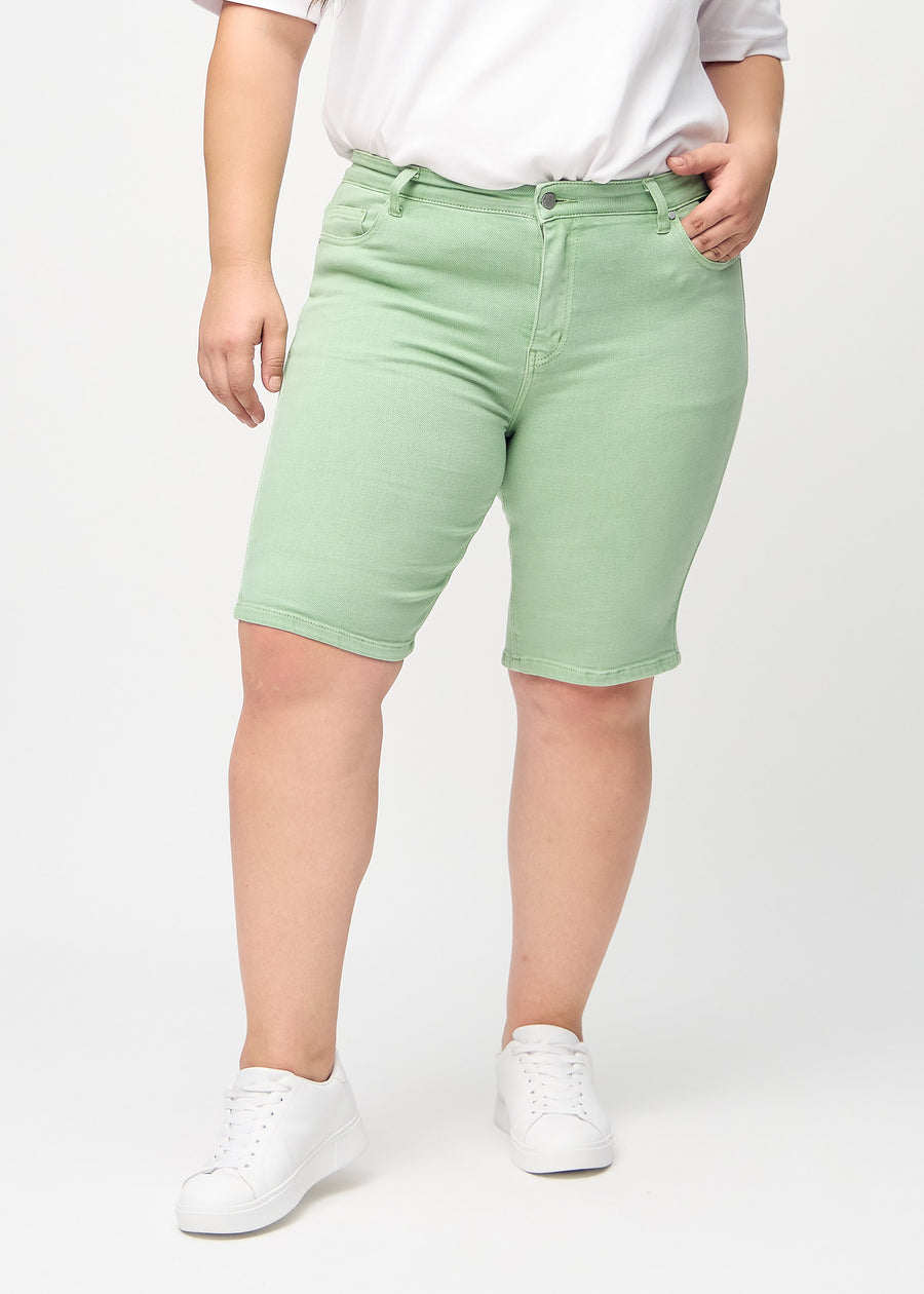 Lysegrønne skinny middle shorts, modellnavn Mints, som sitter tett på låret og slutter rett over kneet på en plus-size-modell, sett forfra.