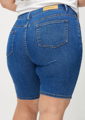 Mørk denim skinny middle shorts sett bakfra på nært hold på en plus-size modell for å vise detaljer.