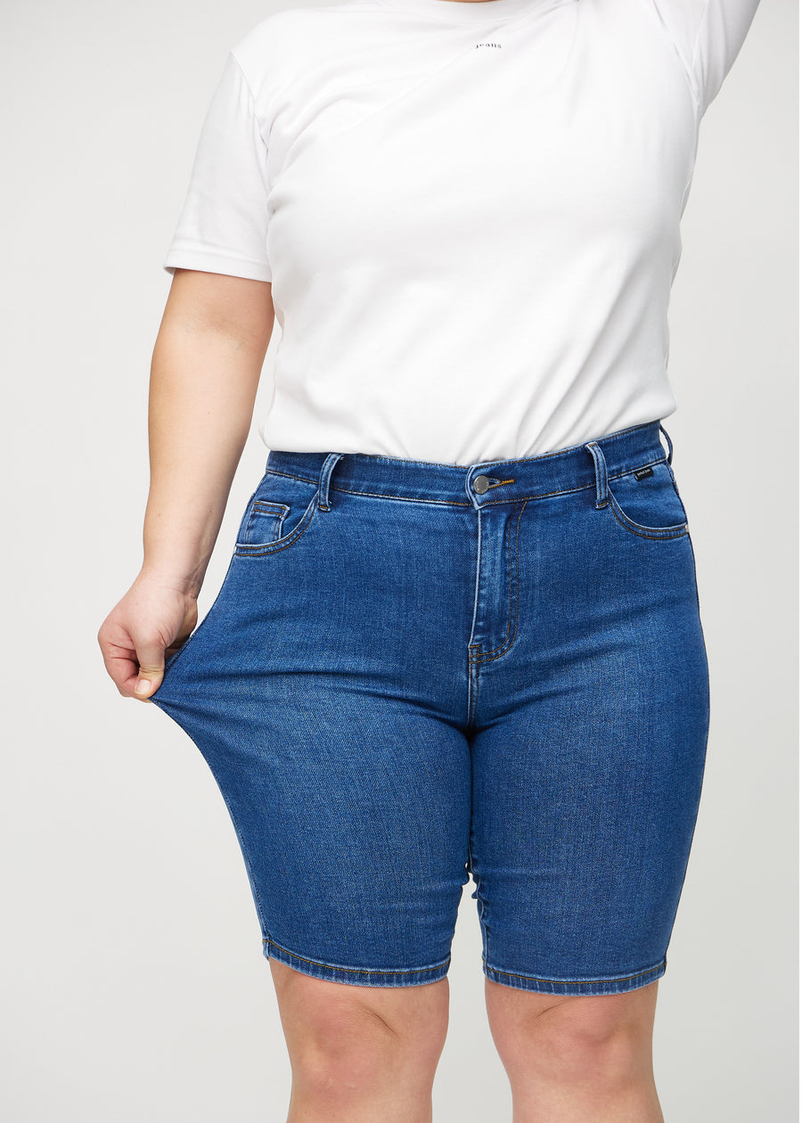 Plus-size modell strekker shortsene ved låret for å vise stretch.