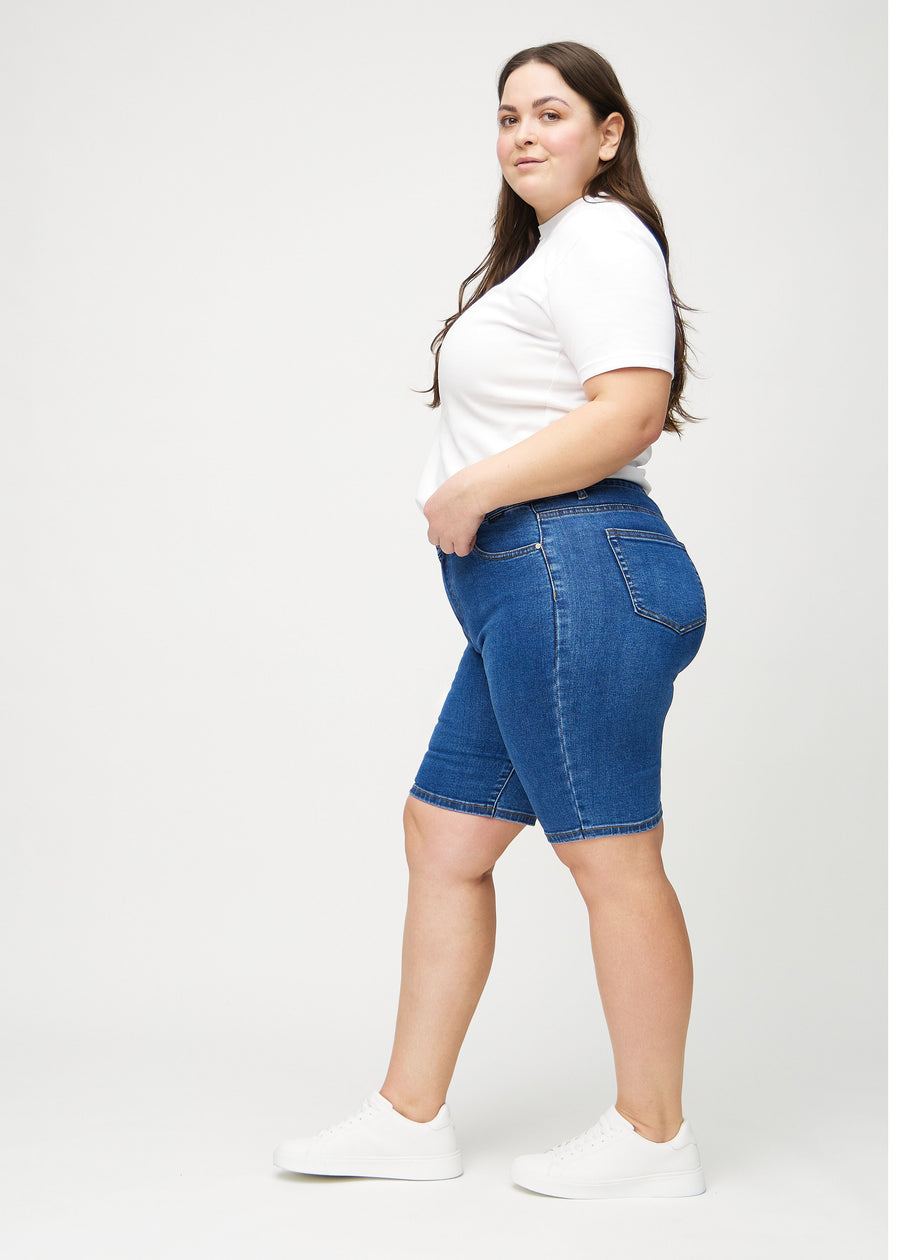 Mørk denim skinny middle shorts sett fra siden på en plus-size modell.