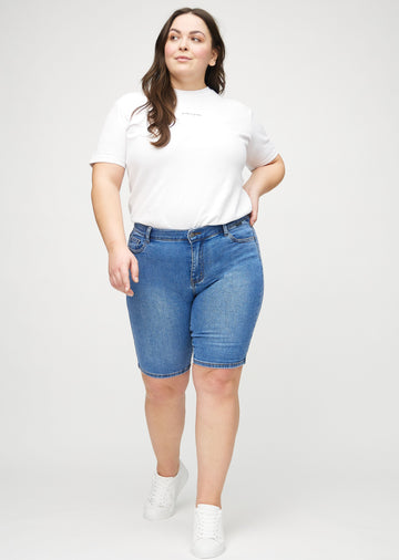 Fullt bilde av en plus-size-modell i denim skinny middle shorts.