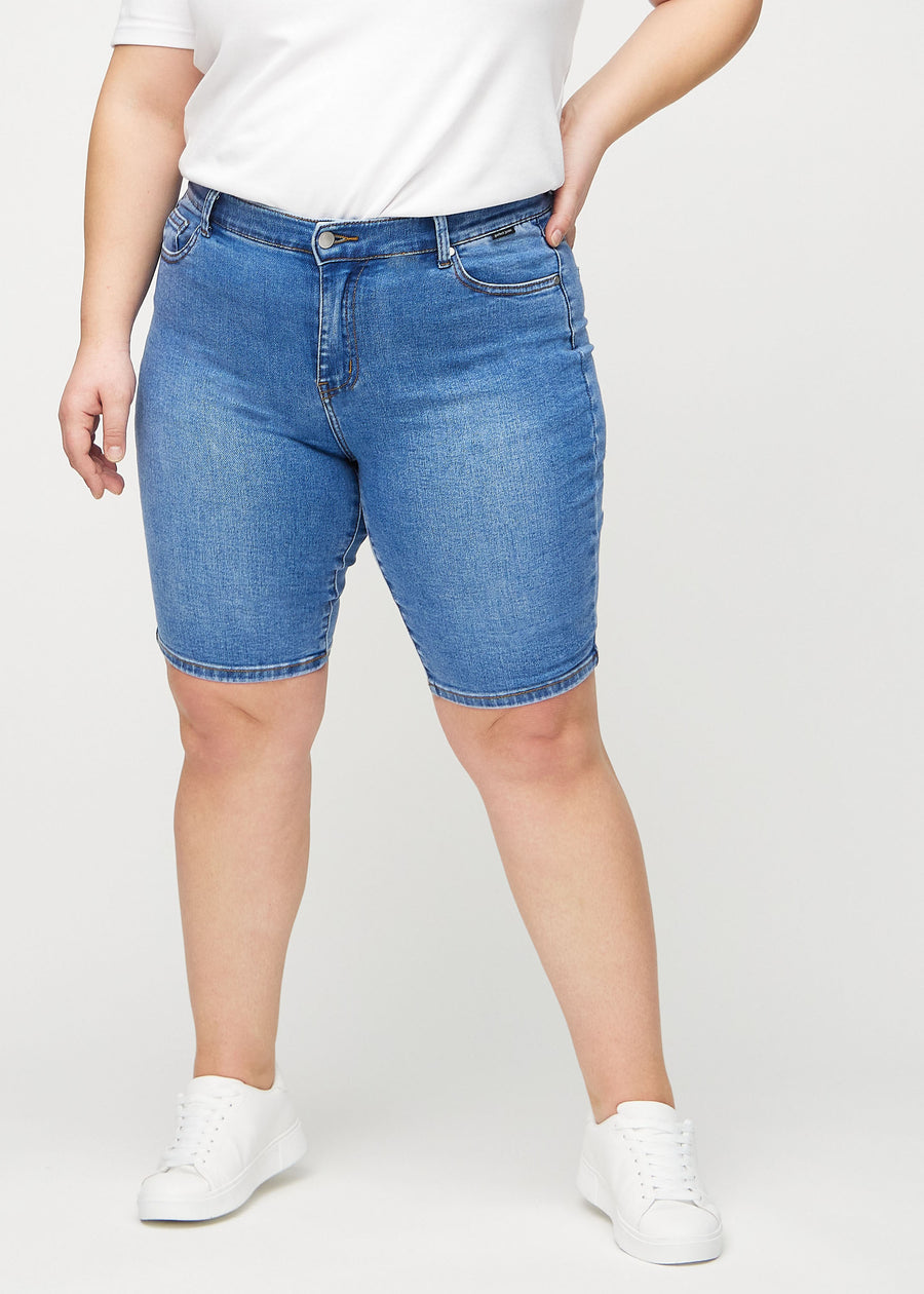Denim skinny middle shorts, modellnavn Rivers, som sitter tett på låret og slutter rett over kneet på en plus-size-modell, sett forfra.