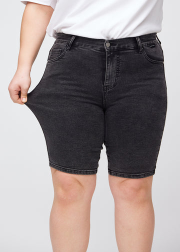 Plus-size modell strekker shortsen ved låret for å vise stretch.