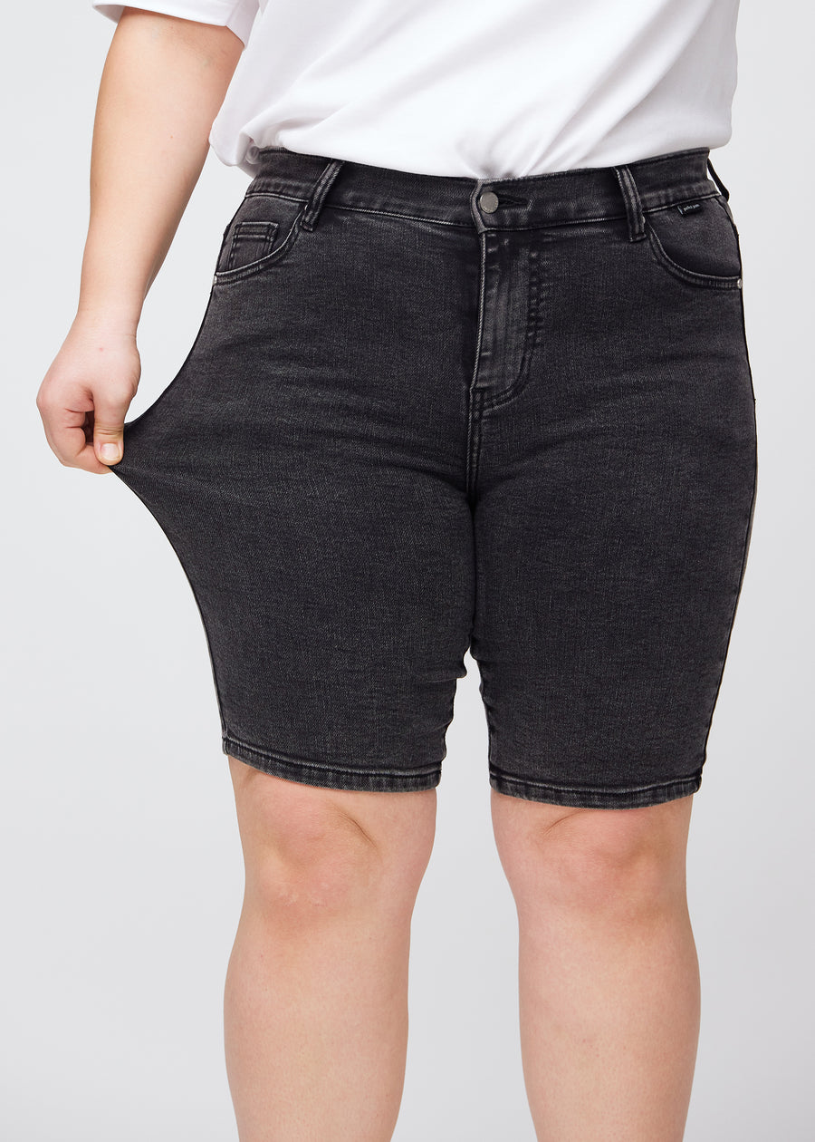 Plus-size modell strekker shortsen ved låret for å vise stretch.