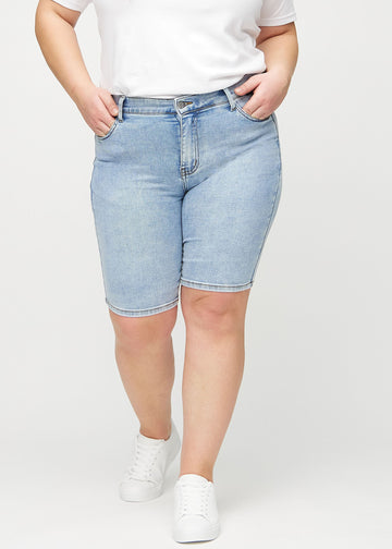 Lys denim skinny middle shorts, modellnavn Waves, som sitter tett til låret og slutter rett over kneet på en plus-size-modell, sett forfra.