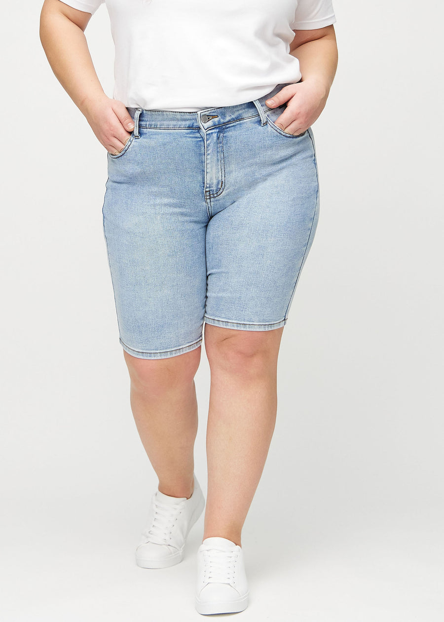 Lys denim skinny middle shorts, modellnavn Waves, som sitter tett til låret og slutter rett over kneet på en plus-size-modell, sett forfra.