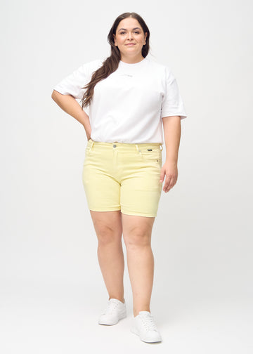 Fullt bilde av en plus-size-modell i lysegule skinny short shorts.