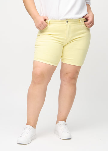 Lysegule skinny short shorts, modellnavn Lemonades, som sitter tett på, og slutter midt på låret på en plus-size-modell, sett forfra.