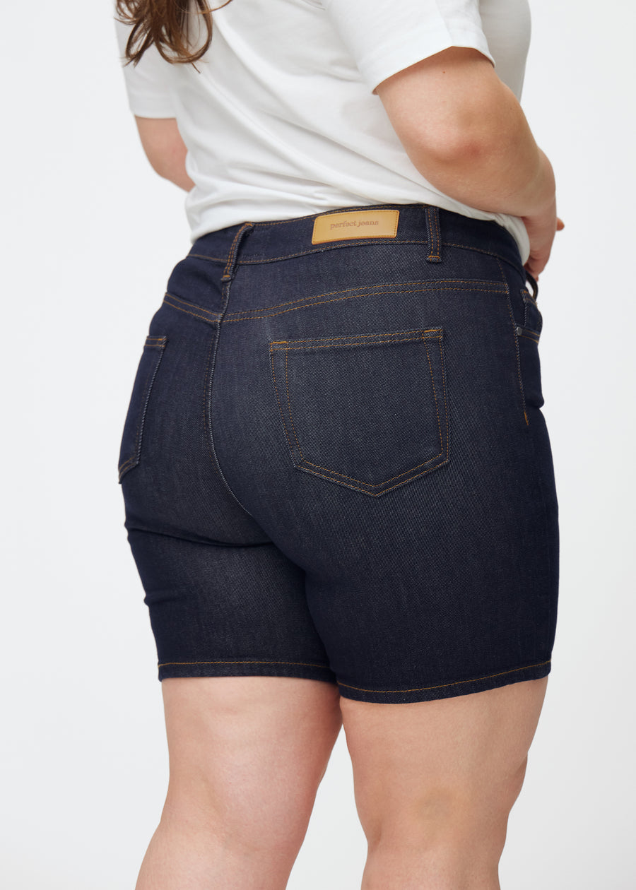 Dyp mørkeblå denimshorts til dame i fargen Midnights sett bakfra i nærbilde på plus-size modell for å vise passform og detaljer.