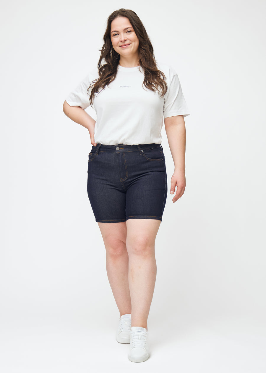 Helbilde av plus-size modell i dyp mørkeblå denimshorts til dame i fargen Midnights med skinny passform.