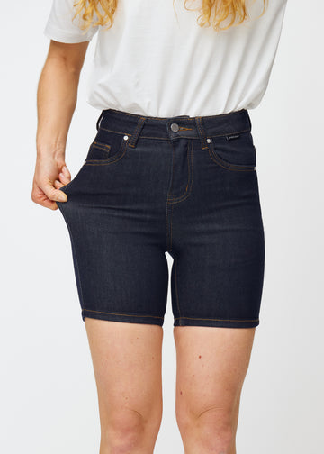 Modell strekker dyp mørkeblå denimshorts til dame i fargen Midnights ved låret for å vise materialets stretch.