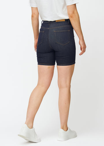 Dyp mørkeblå denimshorts til dame i fargen Midnights sett bakfra, slik at den tettsittende passformen og lengden til midt på låret vises.