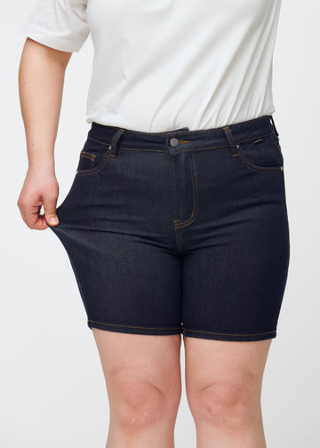 Plus-size modell strekker dyp mørkeblå denimshorts til dame i fargen Midnights ved låret for å vise stretch.